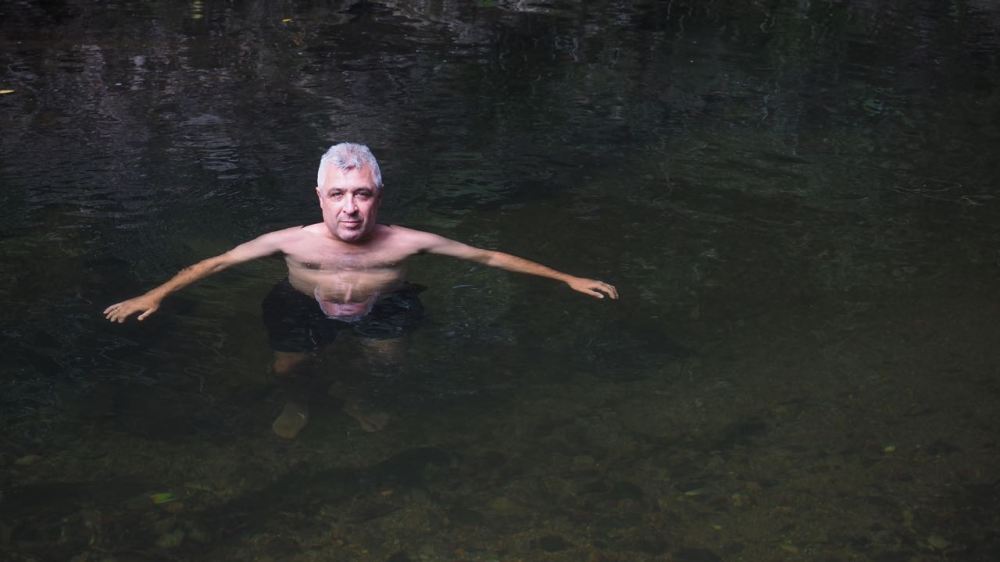 Jordo in dark creek water with his face doubled in reflection